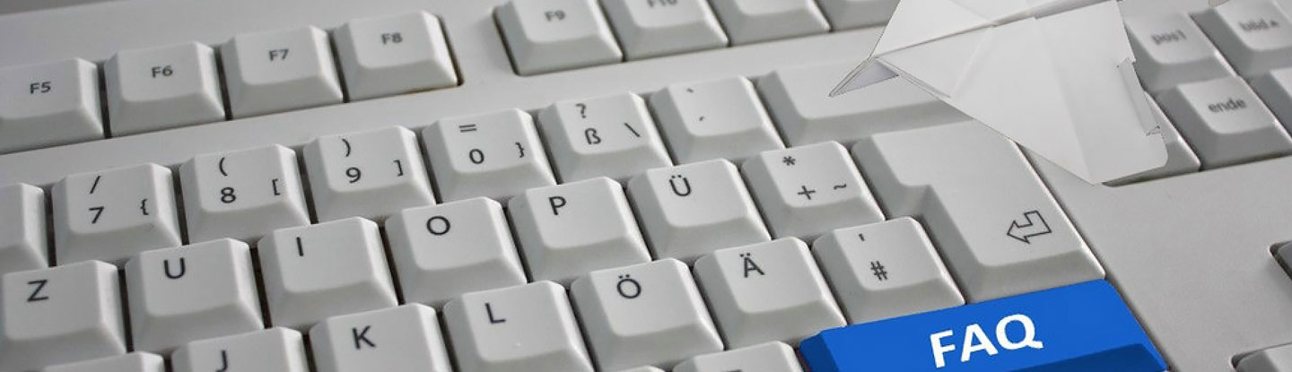 graue Tastatur mit einer blauen Taste mit weißen Buchstaben FAQ, darauf liegt ein weißes Flugzeug aus gefaltetem Papier